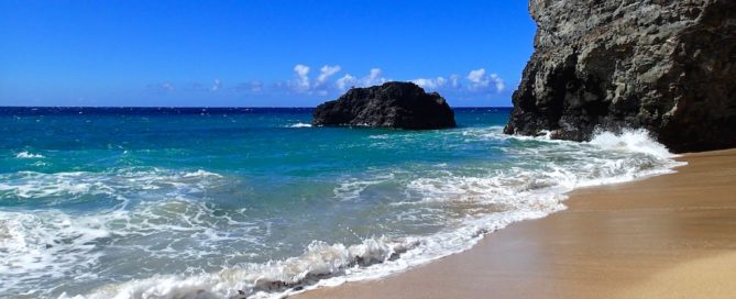 A photo of Kauai's Napali Coast, showcasing a beautiful beach with cliffs rising in the distance.